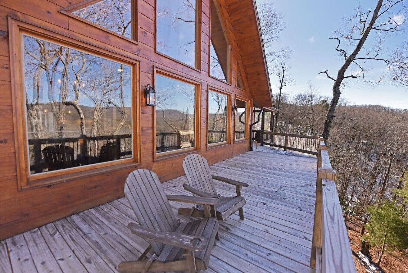Une terrasse en bois, dotée de chaises Adirondack et de grandes fenêtres donnant sur une zone boisée.
