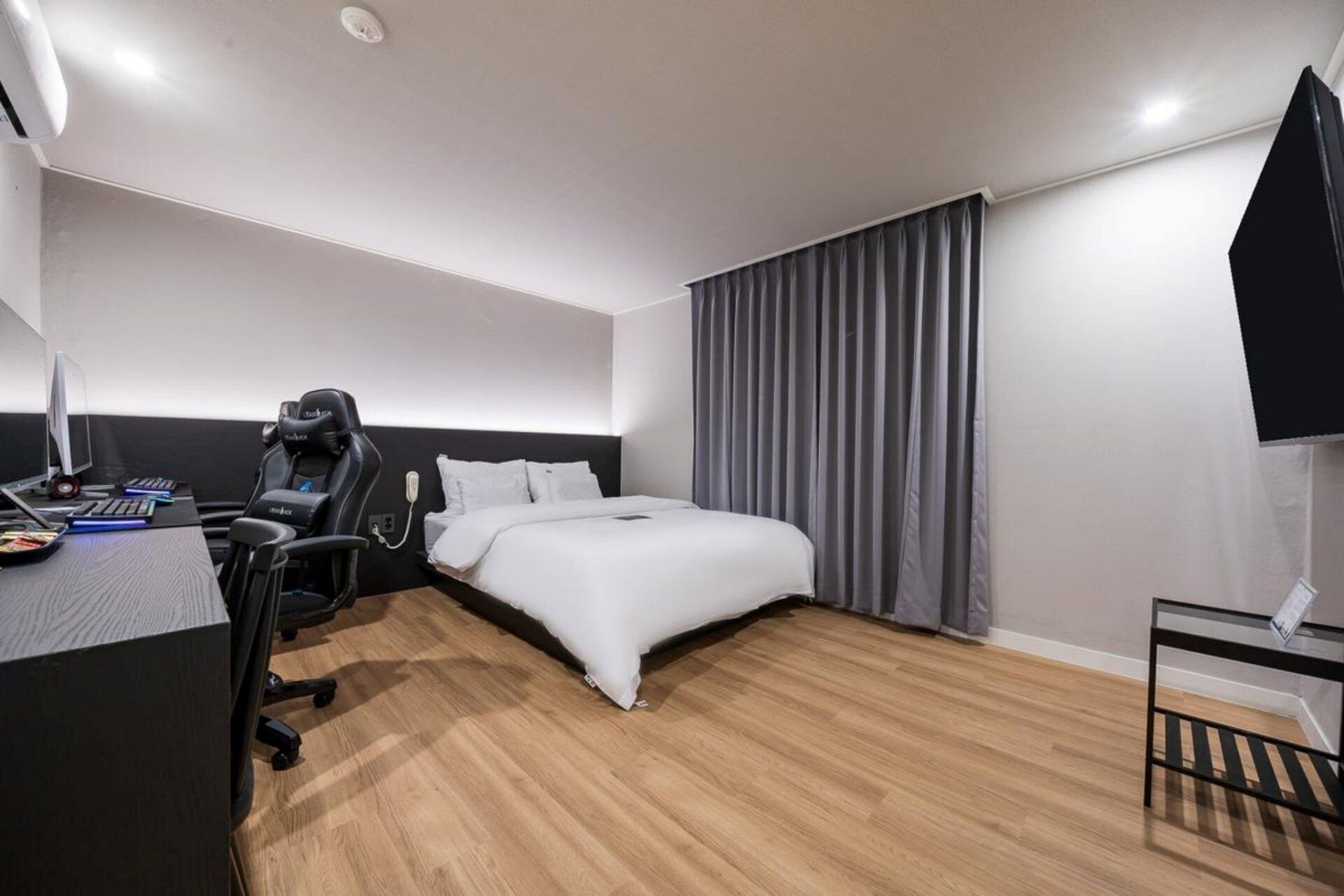 Habitación de hotel con cama, escritorio, computadora, silla y una mesita.