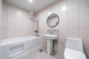 A bathroom with a bathtub, sink, toilet, and a round mirror on the wall. - From H Dongbaek Hotel By Kwon Geoje Gohyeon (Geoje)
