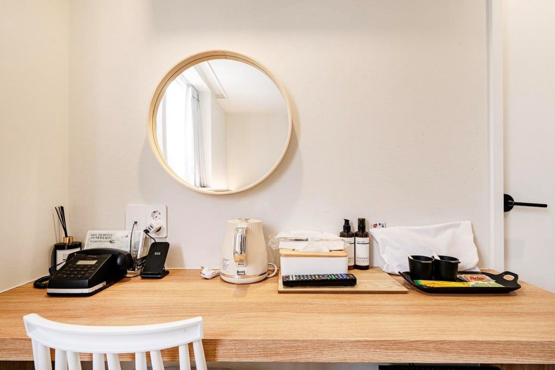Habitación de hotel con un escritorio de madera, un espejo redondo, teléfono, cafetera, control remoto, caja de pañuelos y artículos de aseo.