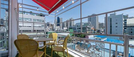 Un balcón con techo rojo, una mesa, sillas y vista de un paisaje urbano.