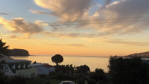 A coastal view with a sunset, houses, and a tree in the foreground.
