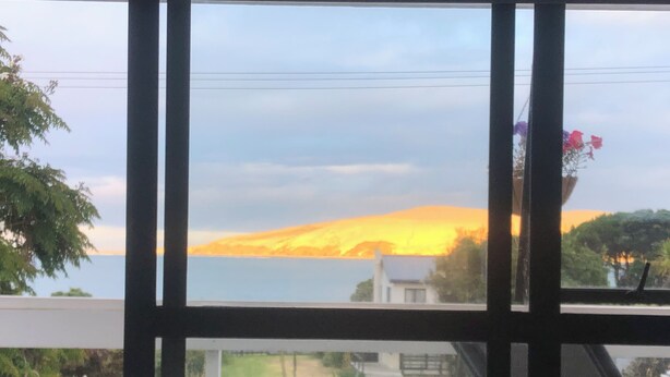 A view from a window with a view of a sunset over a body of water and a hill.
