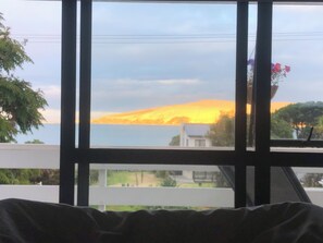 Vista desde una ventana mostrando un atardecer sobre un cuerpo de agua y una colina.