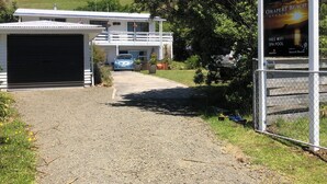A two-story building with a garage, a driveway leading to the entrance, and a sign advertising Omapere Beach Apartments with amenities like free WiFi and a spa pool.