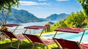 Ein Poolbereich mit roten Liegestühlen und Blick auf Berge und einen See.