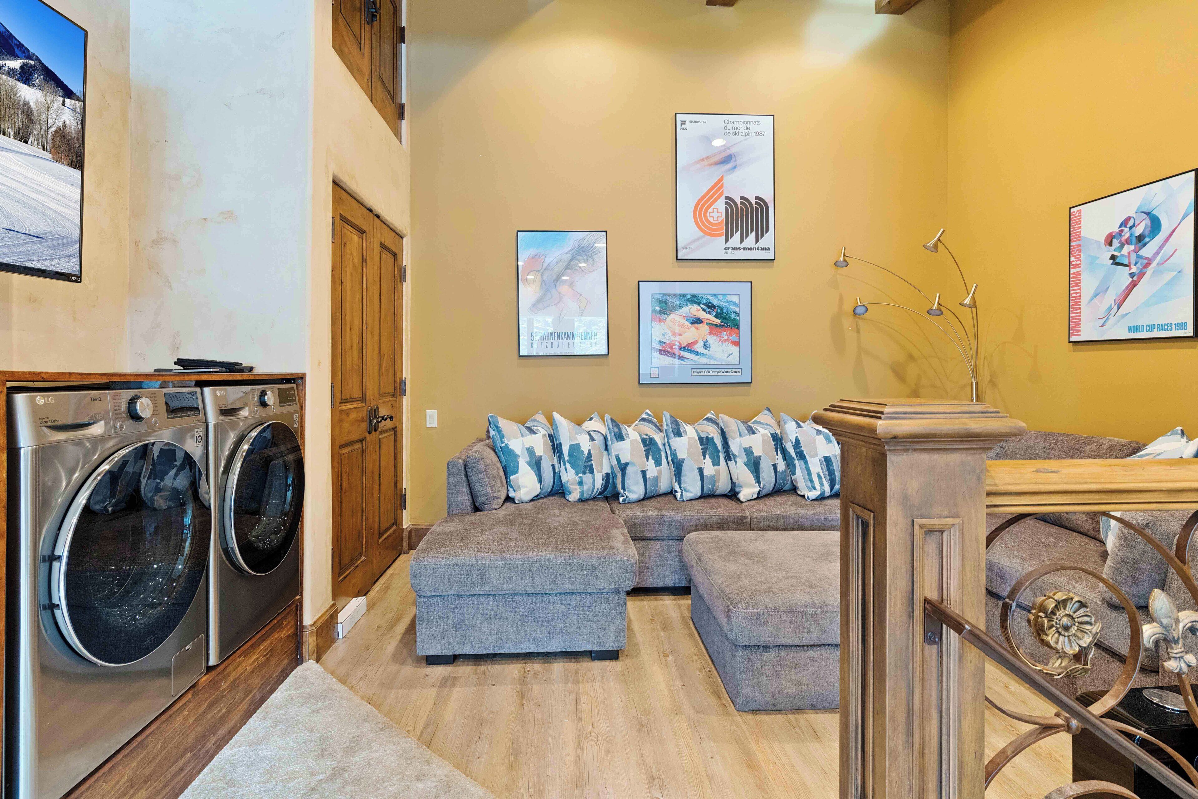 A laundry area with two washing machines, a sofa with patterned cushions, and a staircase with a decorative metal railing.