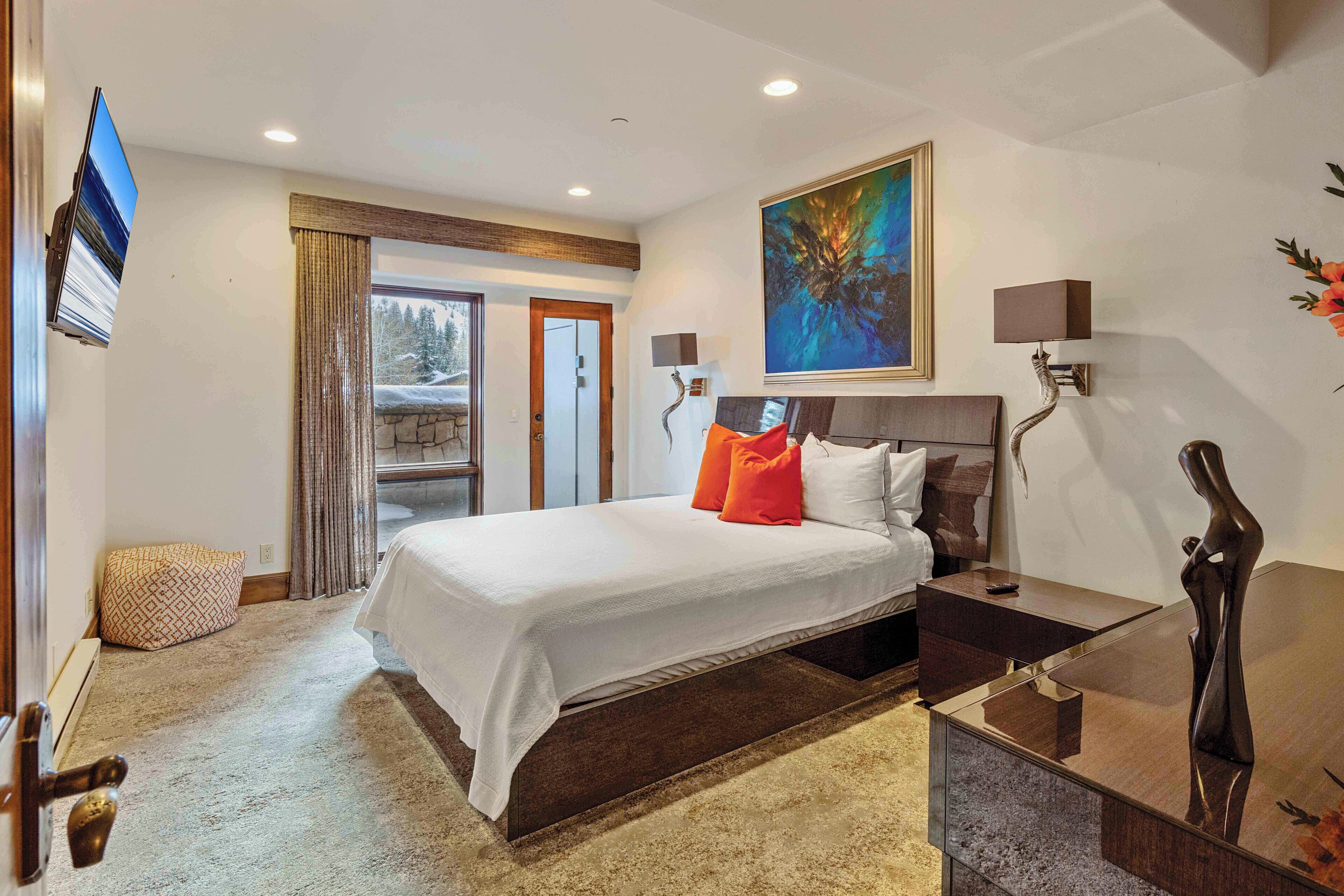 Habitación de hotel con una cama grande, una mesa de centro de vidrio, un cuadro en la pared y vistas al exterior.