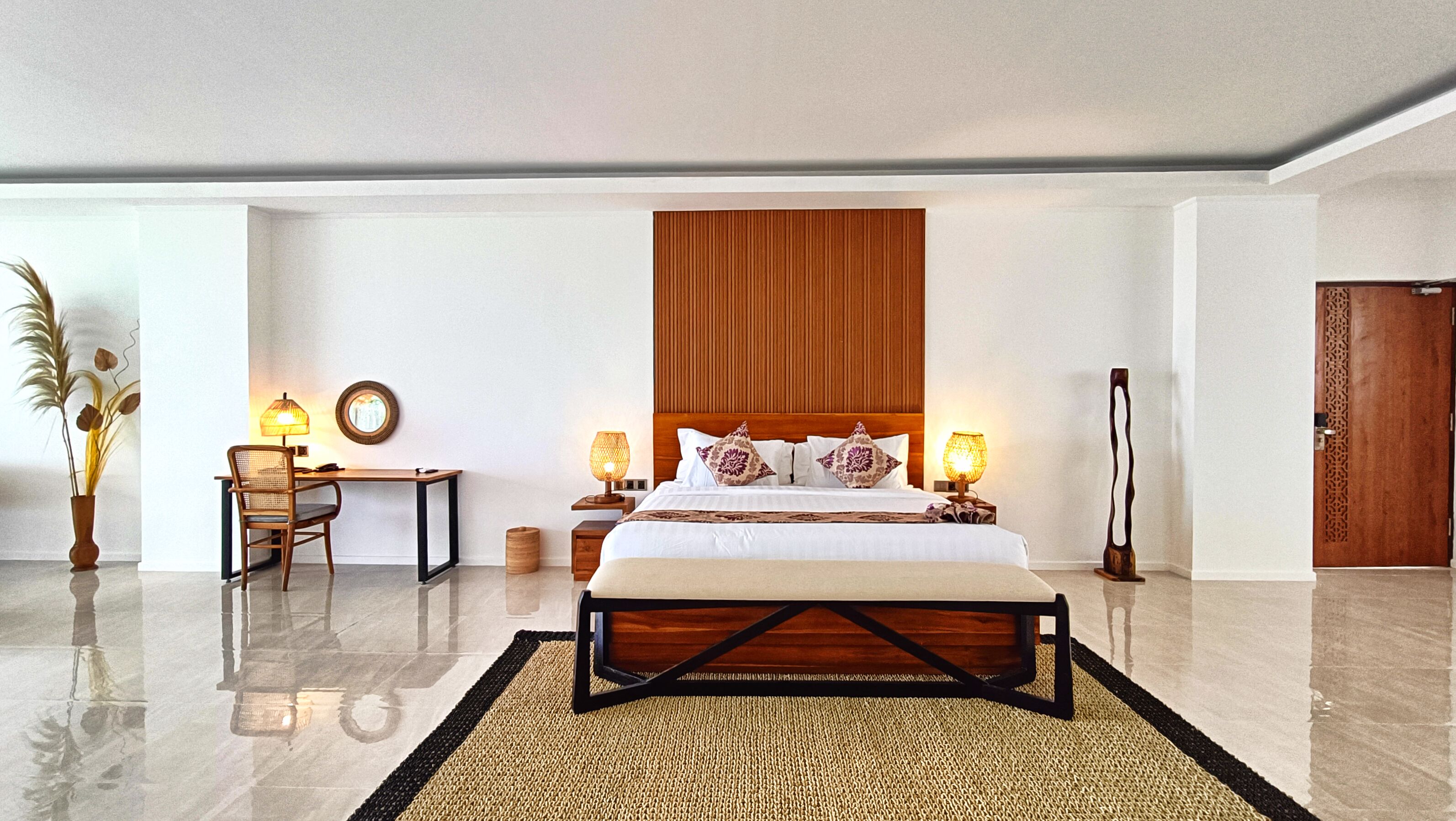 A modern hotel room with a large bed, a desk, two lamps, and a decorative mirror.