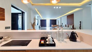 A modern hotel room with a large mirror, a kitchen counter with a coffee maker, tea set, and a tray of condiments.