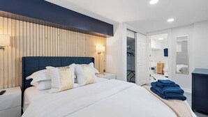 A modern hotel room with a large bed, bedside tables, a wardrobe, and a bathroom visible through an open door.
