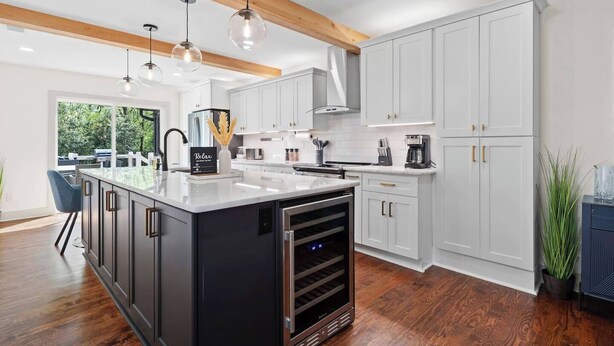 Cocina moderna con una isla central, armarios blancos y una viga de madera en el techo.