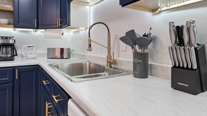 Une cuisine moderne avec des meubles bleu foncé, des appareils en acier inoxydable et un porte-ustensiles noir.