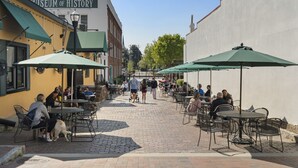 Un café en plein air avec des tables et des chaises, un chien et des gens qui se promènent.
