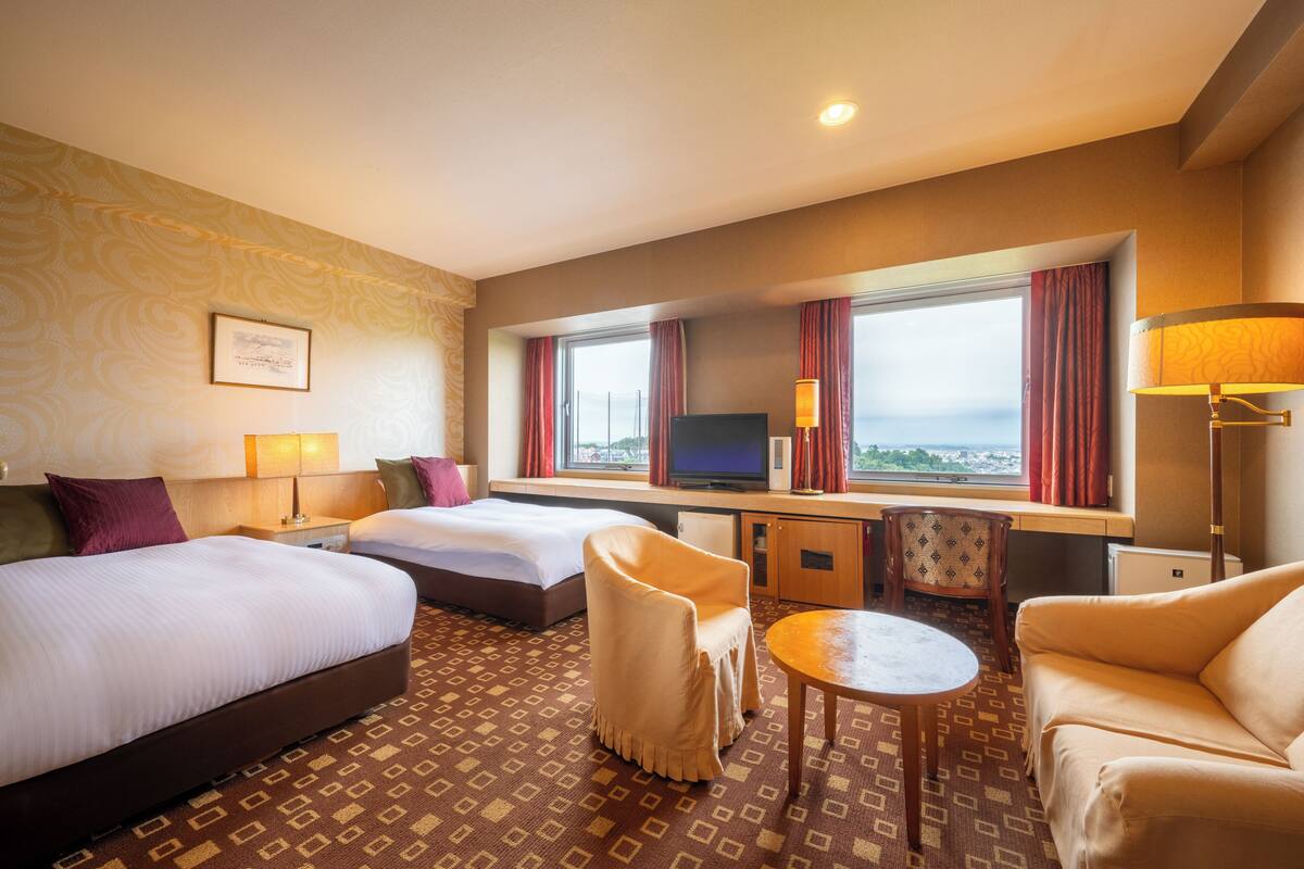 Habitación de hotel con dos camas, un escritorio, un televisor y vista a la ciudad.
