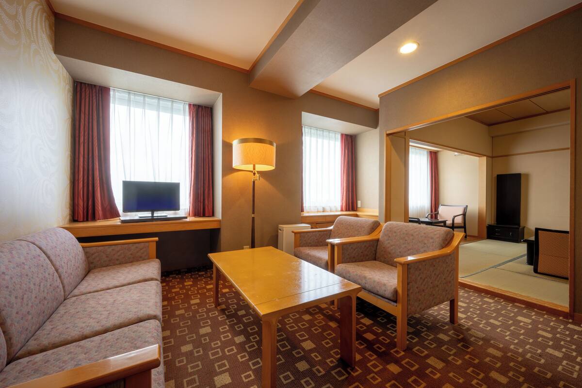 Habitación de hotel con sofá, sillón, mesa, televisor, lámpara y espejo.