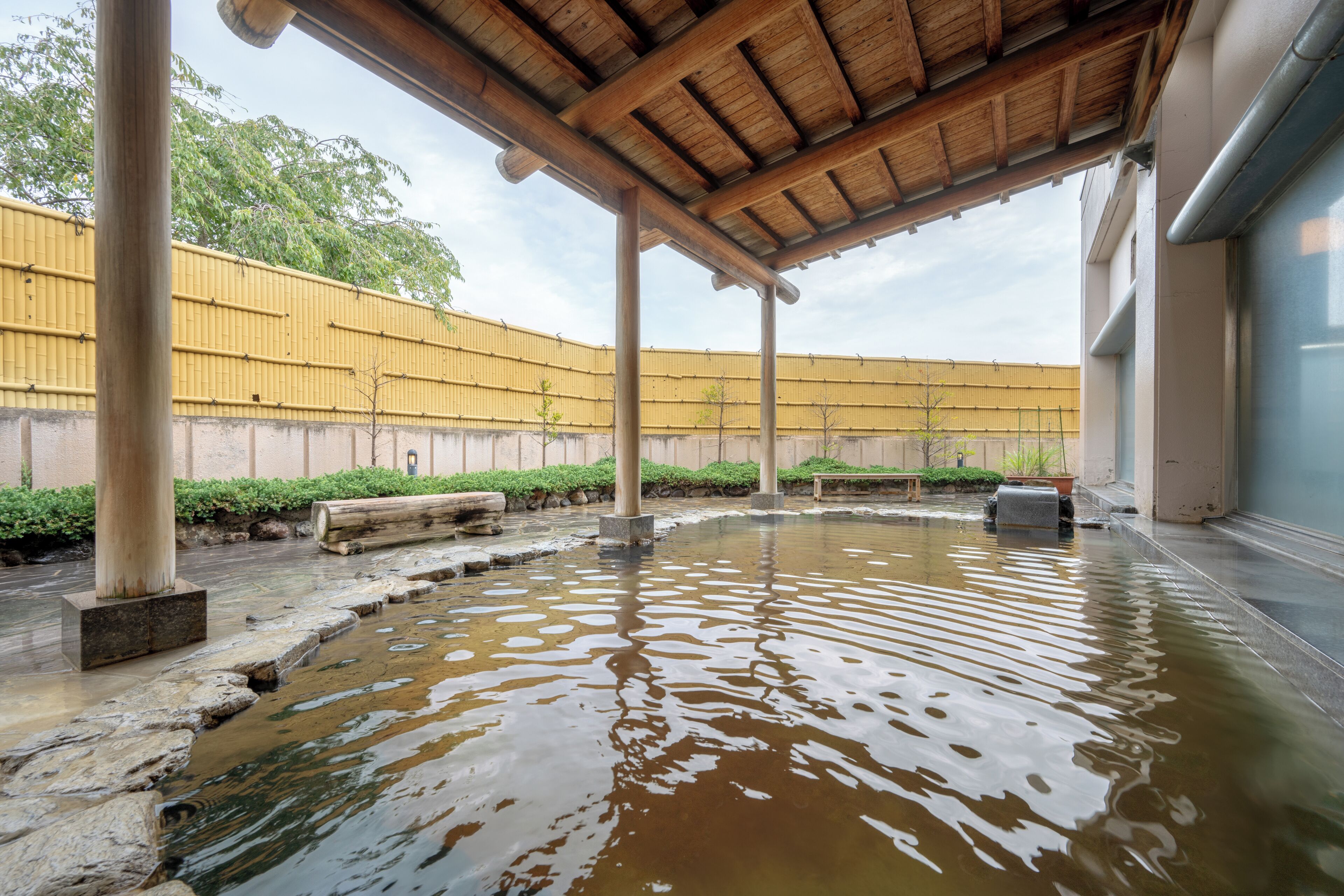 Un espace piscine extérieur abrité, doté de piliers en pierre et d’un toit en bois.