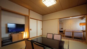 Una habitación de estilo japonés tradicional con suelo de tatami, una mesa baja con sillas, un televisor y un sofá.