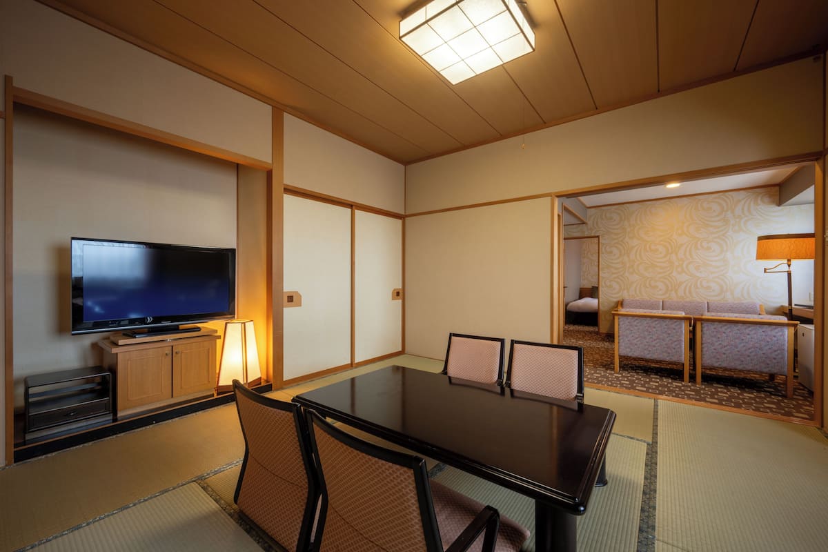 Una habitación de estilo japonés tradicional con suelo de tatami, una mesa baja con sillas, un televisor y un sofá.