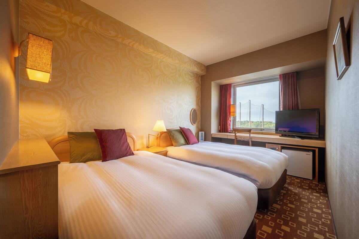 Habitación de hotel con dos camas, televisión, escritorio y ventana con cortinas.