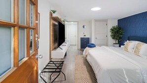 A modern hotel room with a large bed, a desk with a flat-screen TV, a wardrobe, and a small plant. - Marietta Square Suites - Suite3 - Cozy Studio! (Marietta)