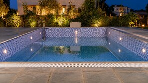 A rectangular swimming pool with a tiled edge, surrounded by a stone deck. - Pavilion Farmstay Udaipur (Udaipur)