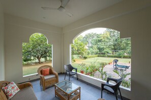 A room with a ceiling fan, large arched windows, wicker furniture, and a glass coffee table. - Pavilion Farmstay Udaipur (Udaipur)