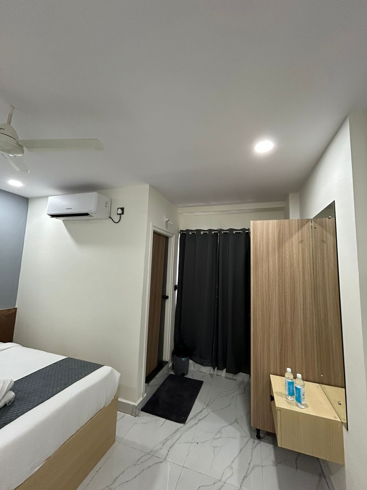 Habitación de hotel con cama, escritorio con espejo, unidad de aire acondicionado y zona de ducha.