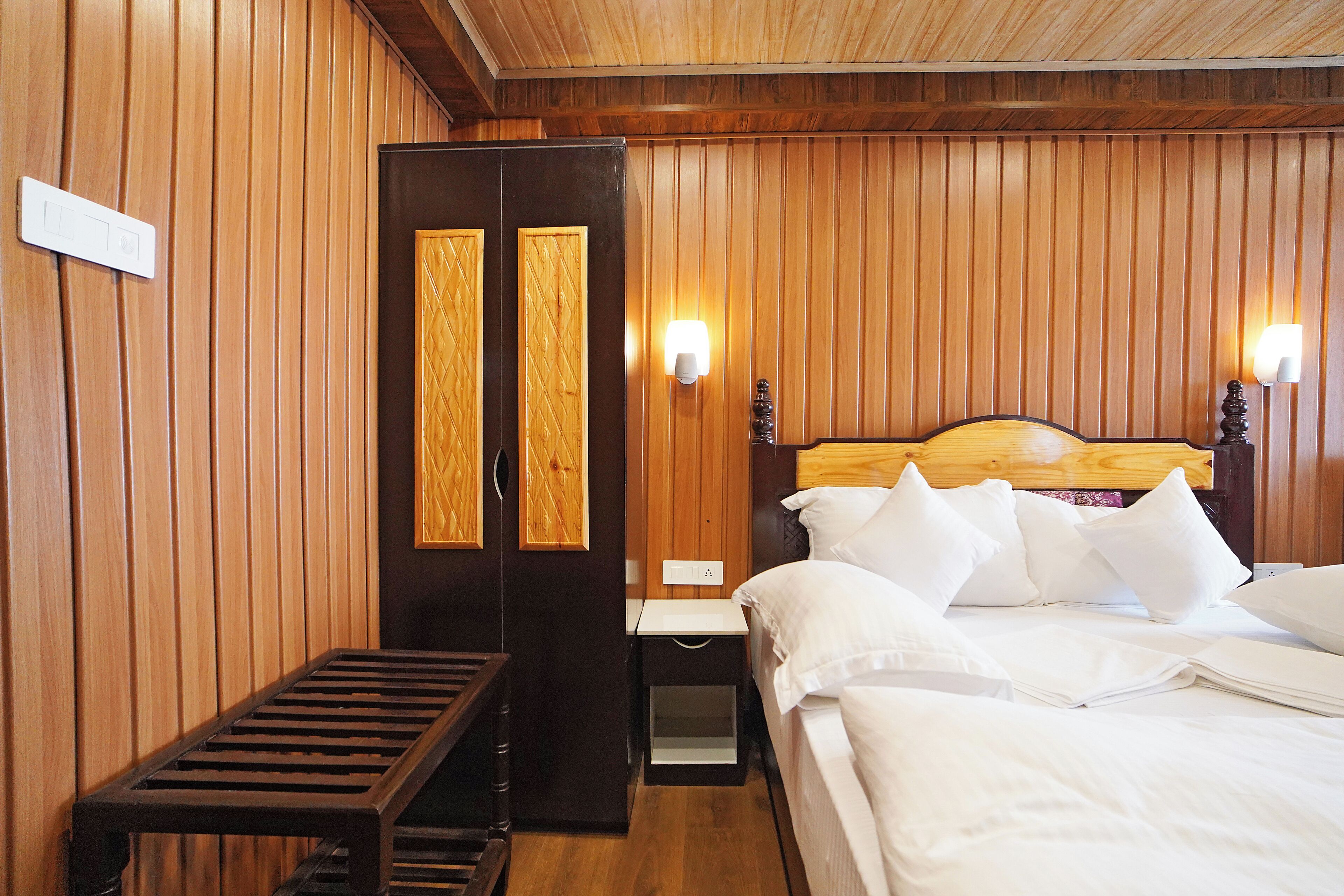 A wooden-paneled room with a bed, bedside tables, and a bench.