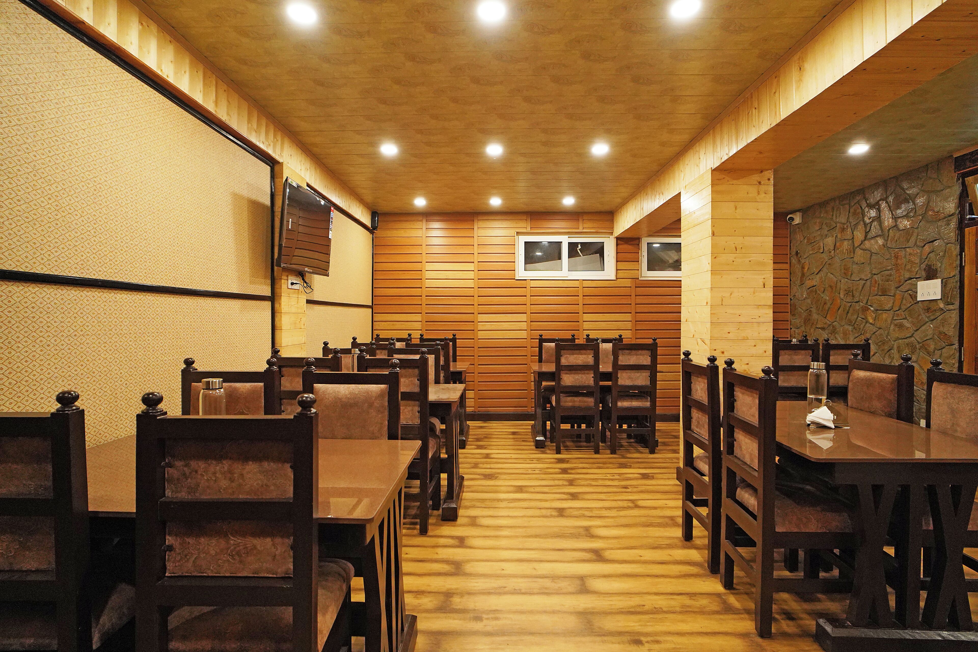 Un restaurant aux murs et au plafond en bois, doté de nombreuses tables et chaises, et dont un mur est habillé de pierres apparentes.