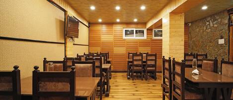 Un restaurant aux murs et au plafond en bois, doté de nombreuses tables et chaises, et dont un mur est habillé de pierres apparentes.
