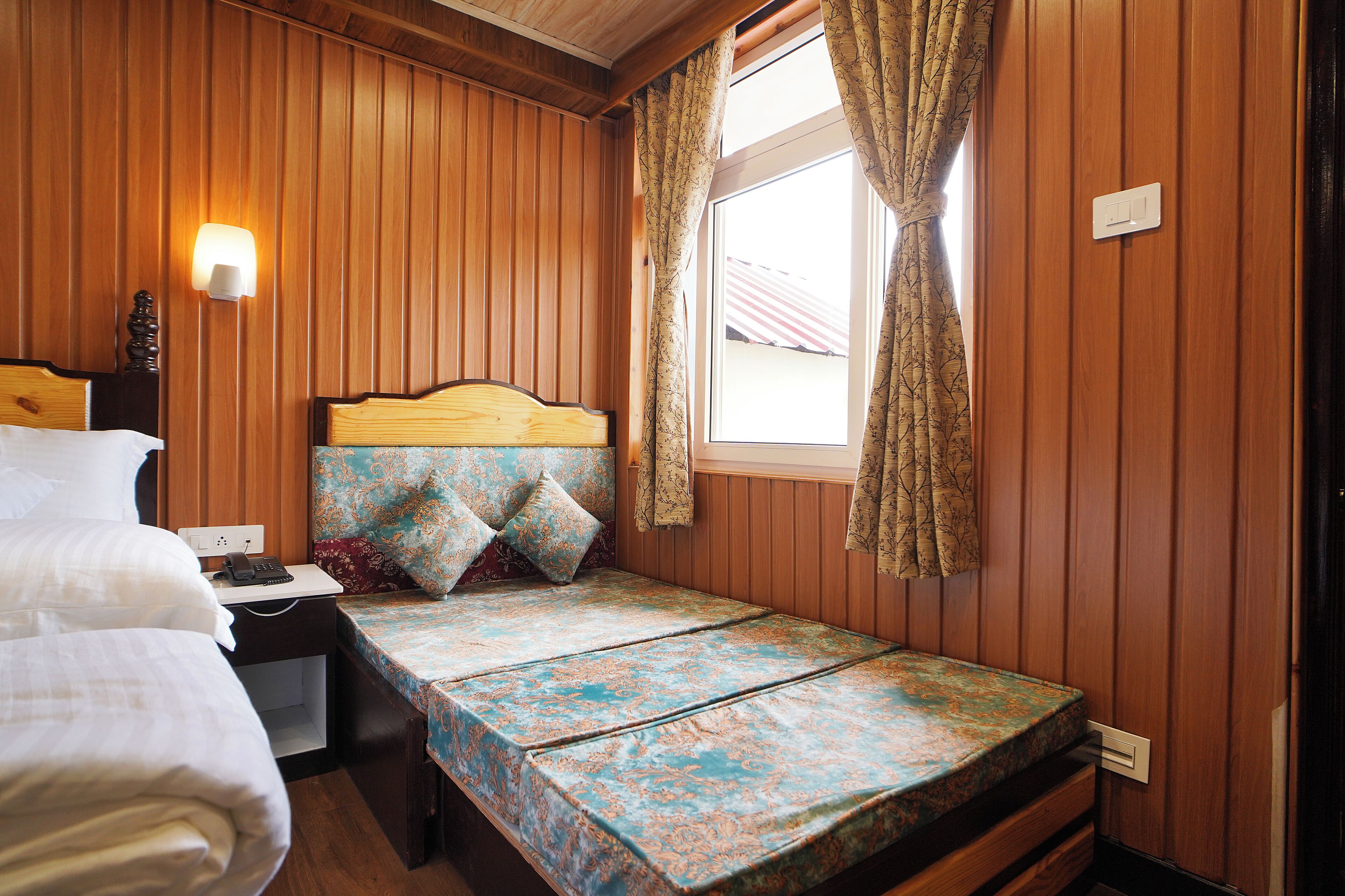 Ein Zimmer mit Holzwänden, einem Bett mit gemustertem Überwurf, einem Nachttisch mit Lampe und einem Fenster mit Vorhängen.
