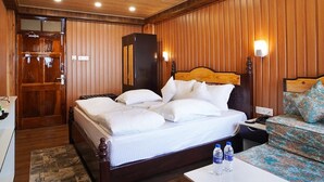 Een hotelkamer met een wand van houten panelen, een bed met witte beddengoed, een nachtkastje met waterflessen en een nachtkastje met een lamp.