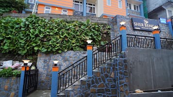 A hotel entrance with a stone wall, a blue and orange facade, and a sign reading "Sher Ben's Absolute Luxury."
