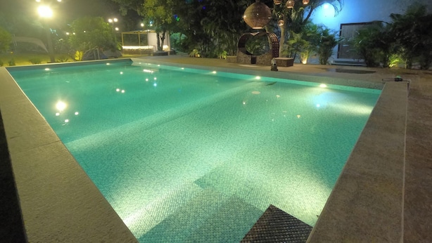 Une piscine éclairée la nuit, entourée d’arbres, avec une zone bien illuminée.