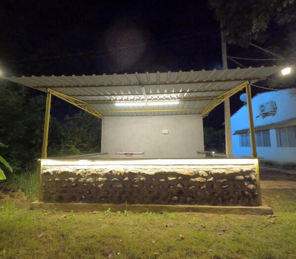 An outdoor covered area with a stone base and a metal roof supported by yellow poles. - Infinite Heavendale (Vikarabad)