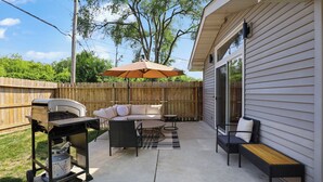 A backyard patio with a grill, outdoor furniture, and a wooden fence.