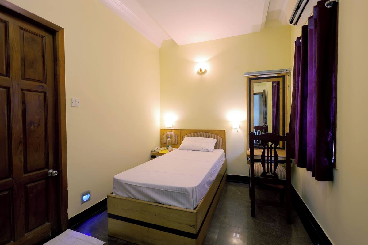 Ein Hotelzimmer mit einem hölzernen Bett, Nachttischlampen, einem Nachttisch, einem Sessel und einem Spiegel.