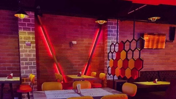 Een restaurant met bakstenen muren, rode neonverlichting en gele en oranje stoelen.