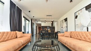 Een moderne woonkamer met twee banken, een ronde tafel en een eethoek op de achtergrond.