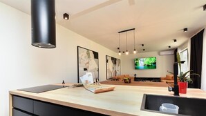 Een moderne keuken met een houten aanrecht, zwarte kasten en een zwarte afzuigkap. Er hangt een televisie aan de muur en er staat een plant aan de rechterkant.