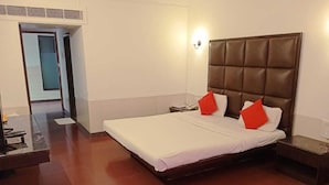 A hotel room with a large bed, two pillows, a nightstand, and a bedside table. - Arnala Beach Resort (Vasai)