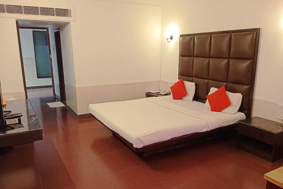 A hotel room with a large bed, two pillows, a nightstand, and a bedside table.