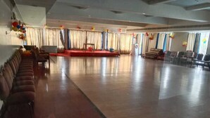 A large hall with a stage, rows of chairs, and a long bench along the walls. - Arnala Beach Resort (Vasai)