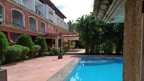 A swimming pool with a red brick pathway, a building with balconies, and lush greenery. - Arnala Beach Resort (Vasai)