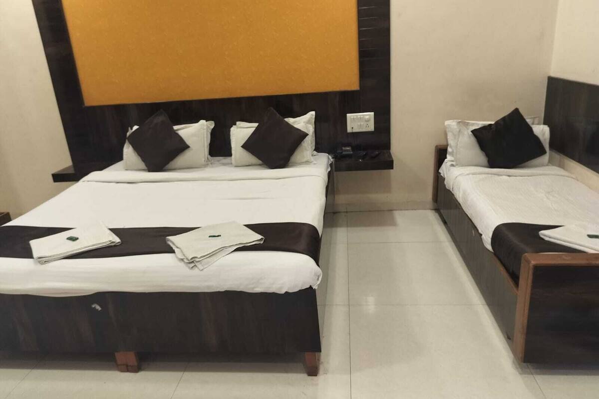 A hotel room with two beds, each with a black headboard, white bedding, and black pillows. There is a nightstand with a lamp between the beds, and a wooden side table next to the right bed.