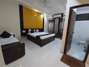 Una habitación de hotel moderna con una cama grande, una cama más pequeña, un baño con ducha y un vidrio que da al área de la ducha.