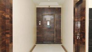 A hallway with wooden doors and a white tiled floor. - Hotel Sachidanand (Rahata)