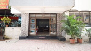 A two-story building with a large entrance, potted plants, and a visible interior space. - Hotel Sachidanand (Rahata)
