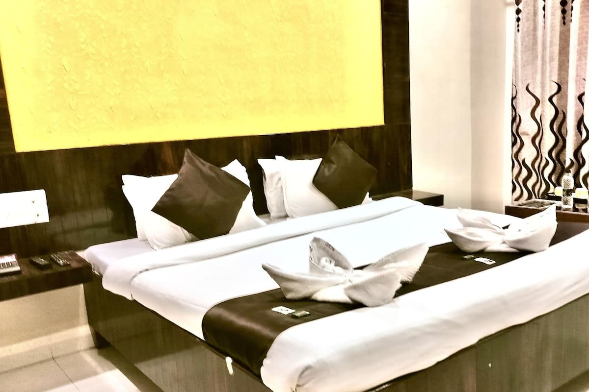 A neatly made bed with white linens and a black accent, a bedside table with a lamp, and a wall-mounted TV.
